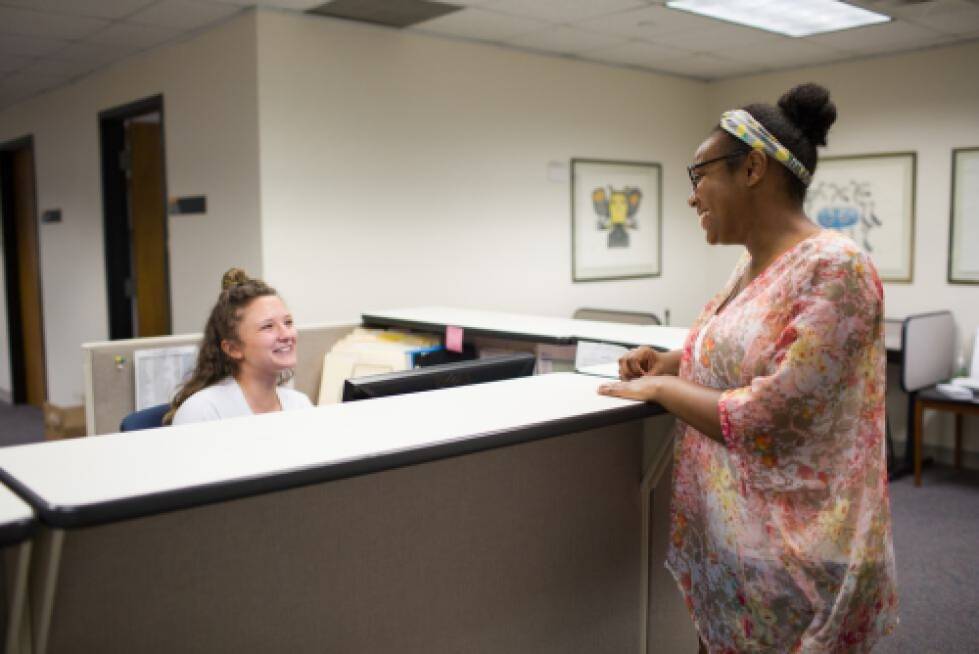Student talking to student working over desk in Psychology Office